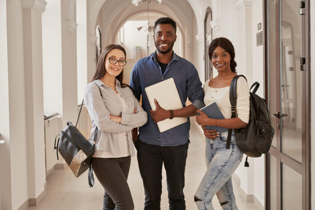 Three students standing a corridor with backpacks and a laptop
